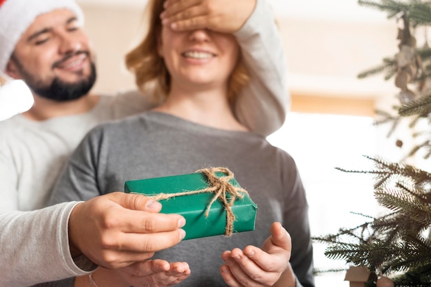 Foto homem cobrindo os olhos da esposa para um presente de natal em casa