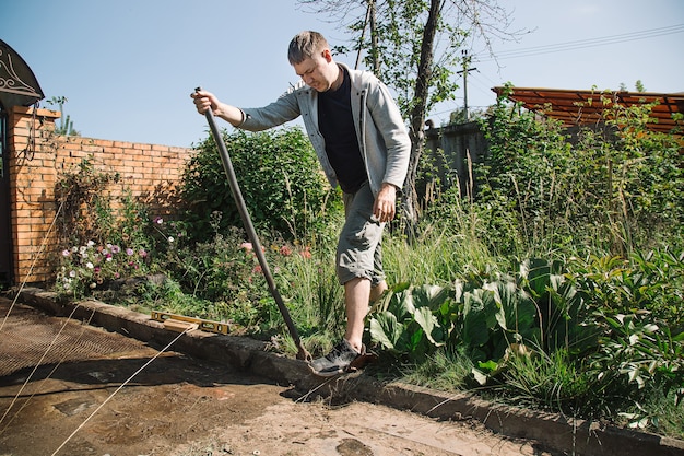 Homem coloca meio-fio para rejuntar o caminho do jardim, trabalhos de construção no terreno do jardim.