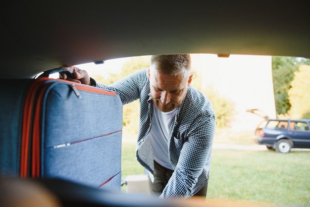 Homem colocando bolsas no porta-malas do carro. pronto para viagens de carro. manhã de sol