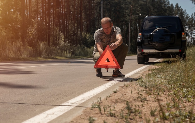 Homem colocando um triângulo de advertência na estrada perto de um carro quebrado