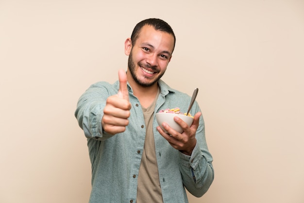 Foto homem colombiano com uma tigela de cereais, dando um polegar para cima gesto e sorrindo