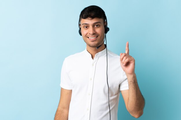 Homem colombiano de telemarketing trabalhando com fone de ouvido isolado, mostrando e levantando um dedo em sinal dos melhores