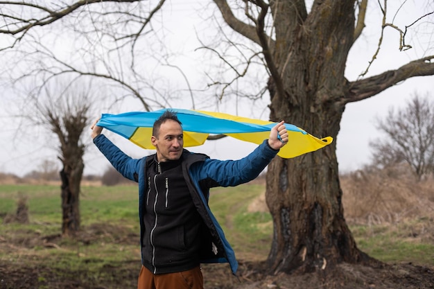 homem com a bandeira da Ucrânia perto da árvore queimada.