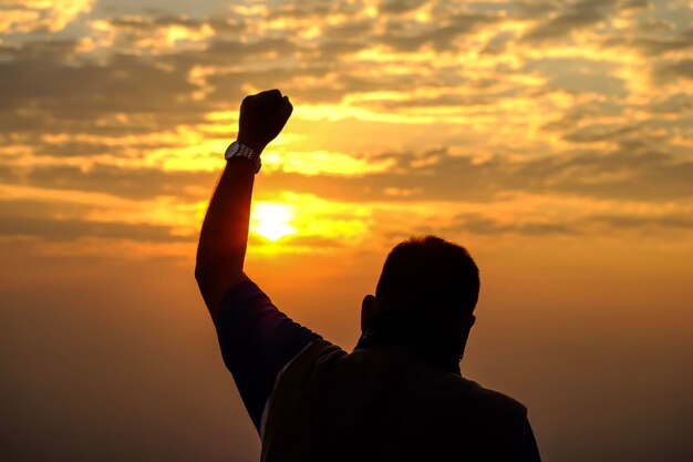 Foto homem com a mão levantada contra o céu nublado durante o pôr do sol