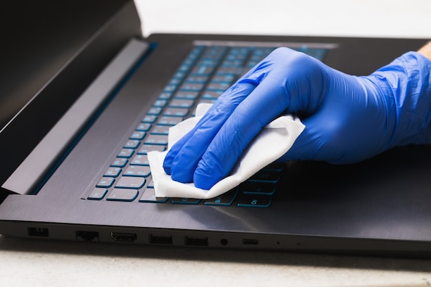 Foto homem com a mão na luva limpa o teclado do laptop com um agente antibacteriano para protegê-lo de bactérias