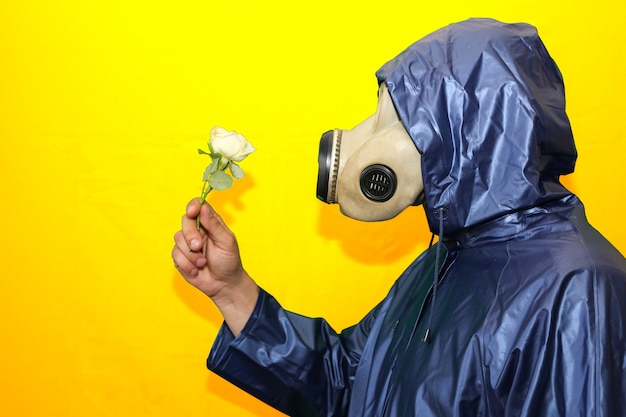 Homem com a máscara de gás segurando flor isolada em fundo amarelo. Influência da radiação. Poluição ambiental. Conceito de Chernobyl. Energia nuclear perigosa. Desastre ecológico.