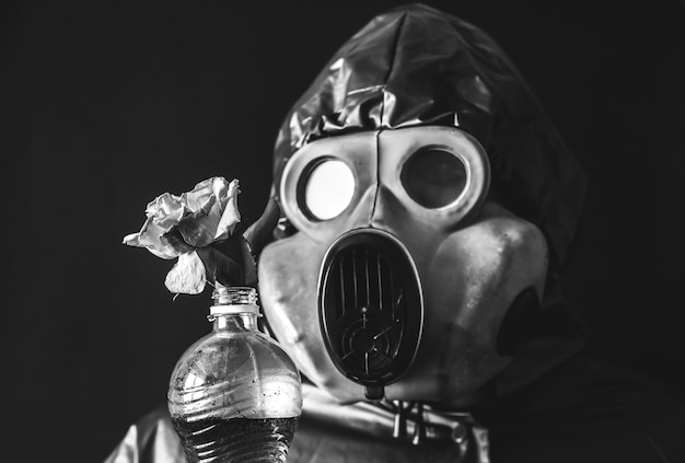 Homem com a máscara de gás segurando uma garrafa de plástico com água suja e flores. Influência da radiação. Poluição ambiental. Conceito de Chernobyl. Energia nuclear perigosa. Desastre ecológico.