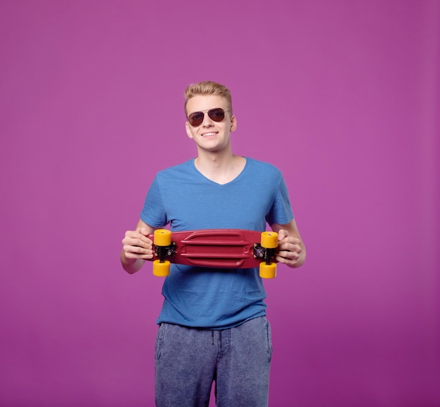 Homem com a prancha do patim na mão sobre fundo roxo, prancha pequena