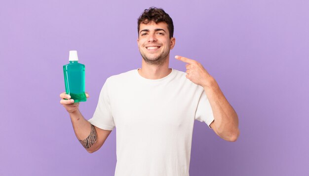 homem com anti-séptico bucal sorrindo com confiança apontando para o próprio sorriso largo, atitude positiva, relaxada e satisfeita