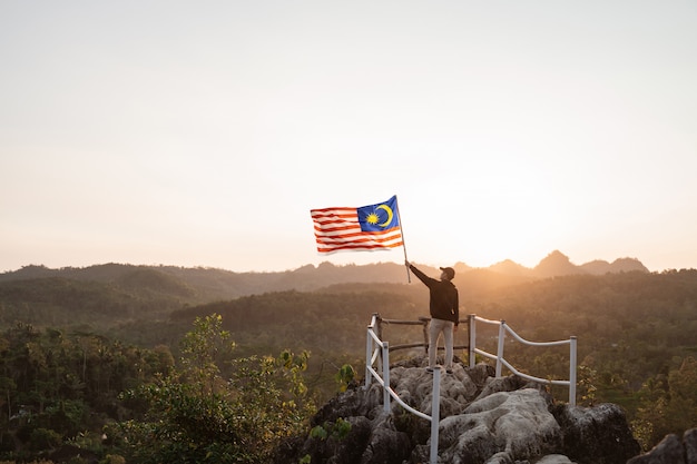 Homem com bandeira da Malásia no topo da montanha