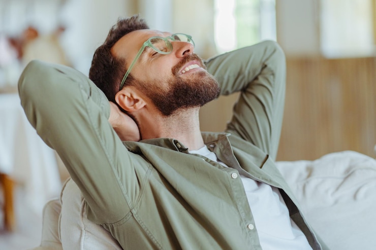 Foto homem com barba bonito usando óculos de moda sentado no sofá e estendendo as mãos no local de trabalho