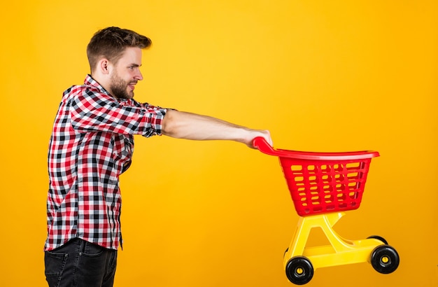 Homem com barba e cabelo penteado na moda carrega carrinho de compras, desconto.