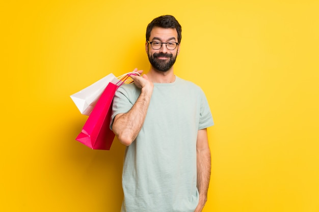 Homem com barba e camisa verde segurando um monte de sacos de compras