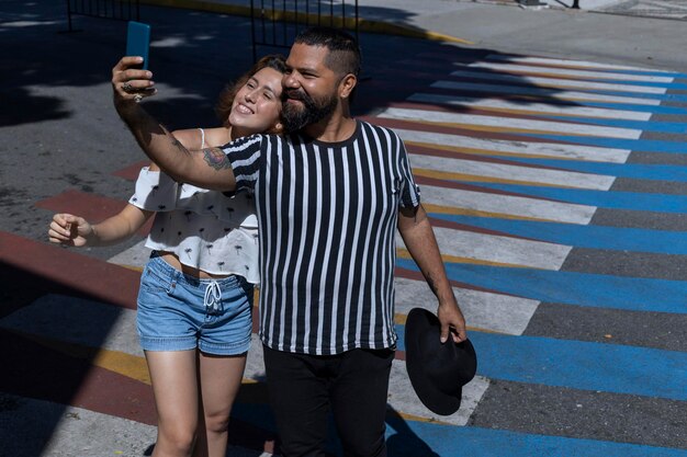 Homem com barba e chapéu ao lado de uma jovem latino-americana tira um retrato de si mesmo enquanto caminha pela cidade durante sua viagem de férias Conceito de férias