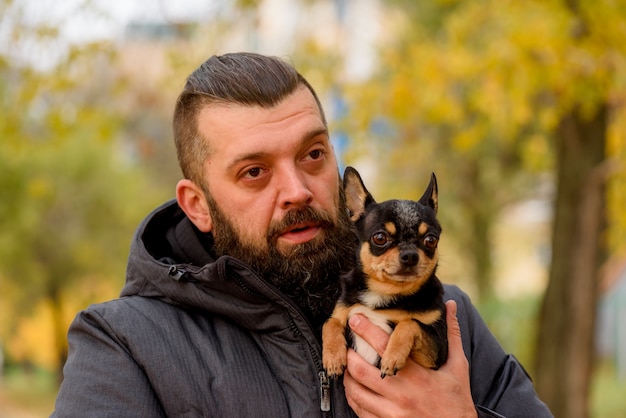 Homem com barba e chihuahua. um homem no parque com seu amado animal de estimação nos braços. cara com cachorro