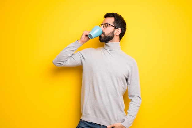 Homem com barba e gola alta segurando uma xícara de café quente