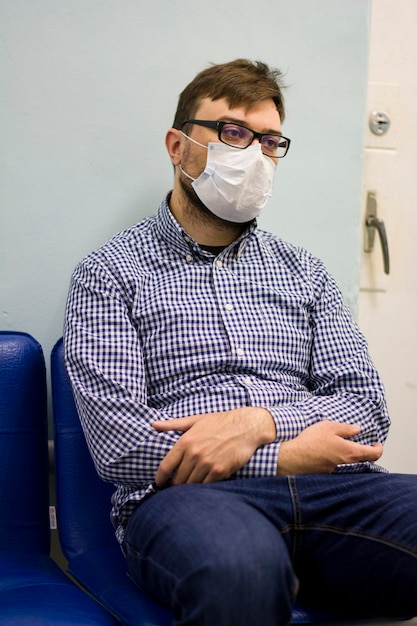 Homem com barba e óculos de camisa senta-se em uma máscara de proteção médica durante o coronovírus