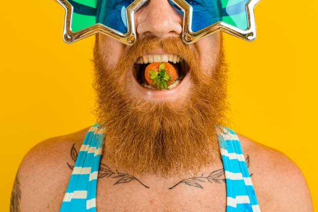 Homem com barba e óculos de sol comendo morango