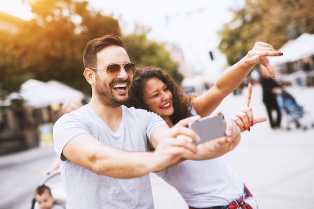 Homem com barba e óculos de sol sorrindo enquanto tirava uma foto com uma linda jovem.