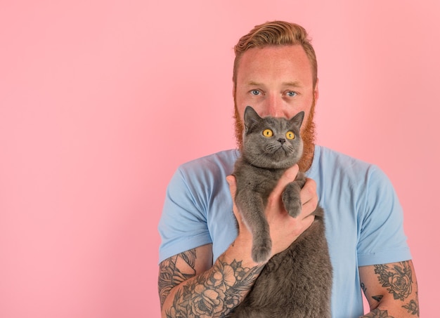 Homem com barba e tatuagens acariciando um gato cinza