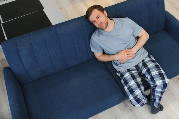 Foto homem com barba se sentindo mal com dor de estômago enquanto está sentado em um sofá em casa