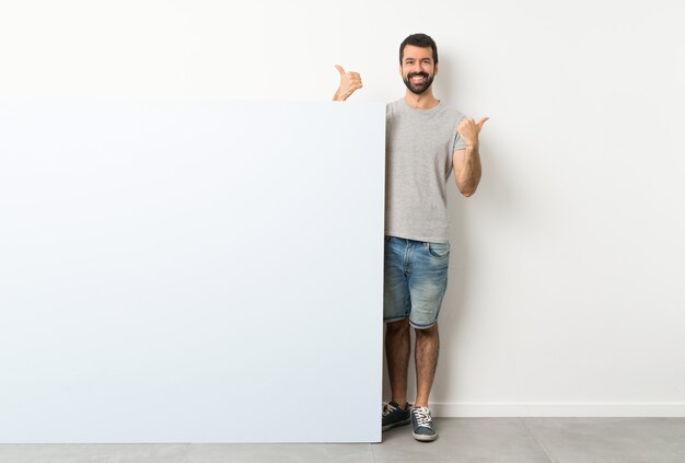 Homem com barba segurando um grande cartaz vazio azul com polegares para cima