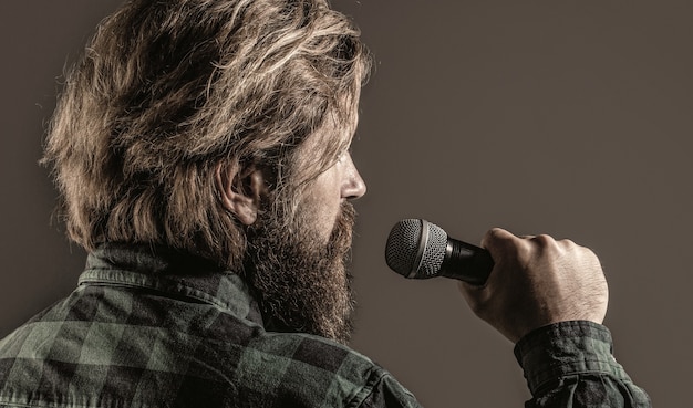 Homem com barba segurando um microfone e cantando. Um homem barbudo no karaokê canta uma música em um microfone. Homem vai ao karaokê.