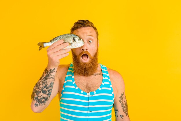 Homem com barba, tatuagens e maiô pegou um peixe