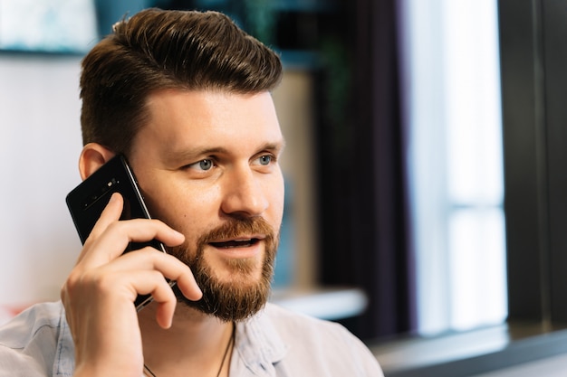 Homem com barba trabalhando remotamente enquanto fala com seu telefone móvel