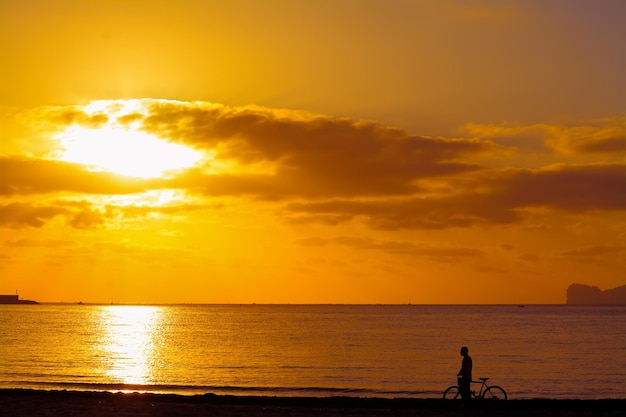 Homem com bicicleta à beira-mar ao pôr do sol Filmado na Sardenha Itália