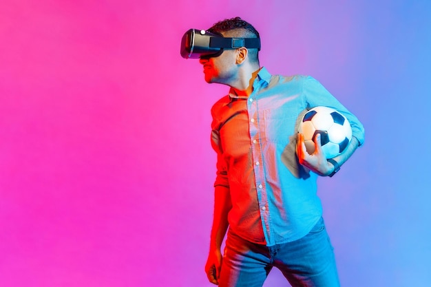 Homem com bola de futebol usando óculos de realidade virtual olhando atentamente ao lado do espaço de cópia para anúncio