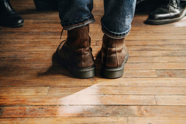 Homem com botas de couro marrom em pé sobre um piso de madeira