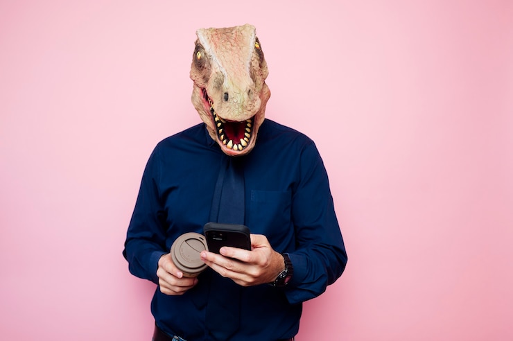 Foto homem com cabeça de dinossauro com uma xícara de café e um smartphone.