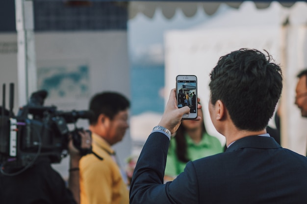 Homem com cabelo escuro, tirando foto de pessoas no smartphone