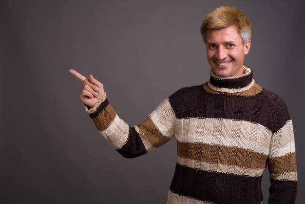 Homem com cabelo loiro e suéter de gola alta isolado contra uma parede cinza