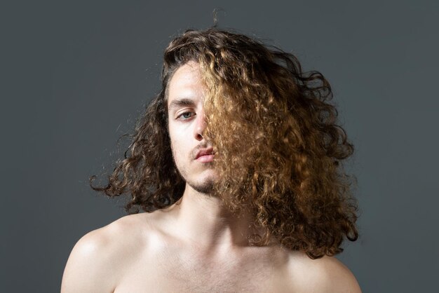 Homem com cabelo longo cacheado, corte de cabelo, estilo de cabelo moderno. Feche o retrato do modelo masculino com cabelo comprido. Conceito de cuidados de saúde e cuidados com os cabelos.