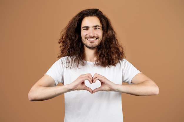 Homem com cabelos longos formando as mãos em retrato de estúdio de coração