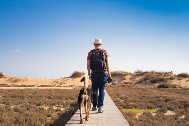 Homem com cachorro andando no caminho de madeira na praia e olhando para a distância do oceano.