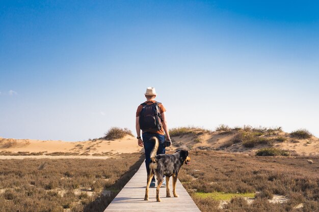 Homem com cachorro andando no caminho de madeira na praia e olhando para a distância do oceano.