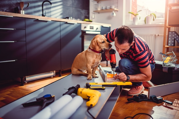 Homem com cachorro construindo armários de cozinha e usando uma furadeira sem fio