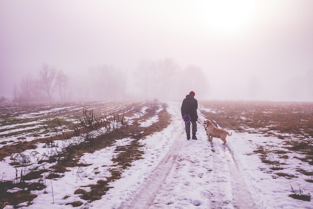 Homem com cachorro Labrador retriever andando no campo no inverno Campos cobertos com a primeira neve