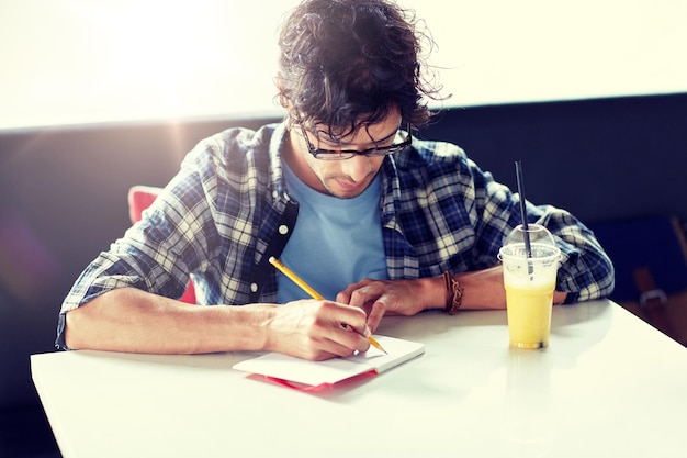 Foto homem com caderno e suco escrevendo no café