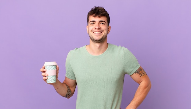 Homem com café sorrindo feliz com uma mão no quadril e atitude confiante, positiva, orgulhosa e amigável