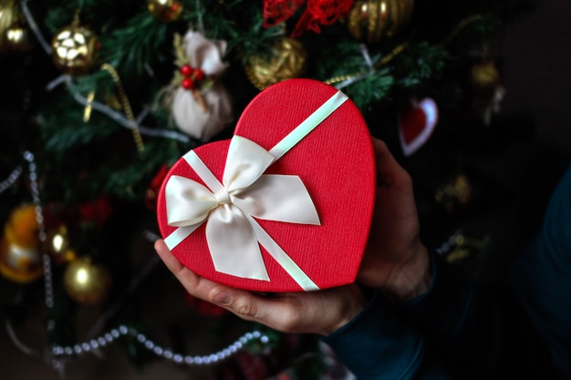 Homem com caixa de presente de coração vermelho nas mãos com decoração de árvore de Natal