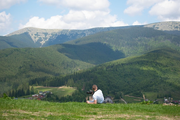 Homem com câmera encontra-se em uma colina e fotografia natureza. Dia de verão