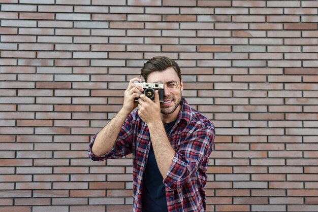 Homem com câmera fotográfica retrô Fashion Travel Lifestyle ao ar livre em pé contra o fundo da parede de tijolo.