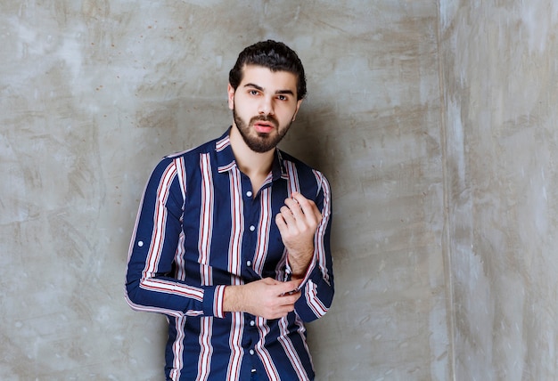 Homem com camisa listrada, fechando a camisa.