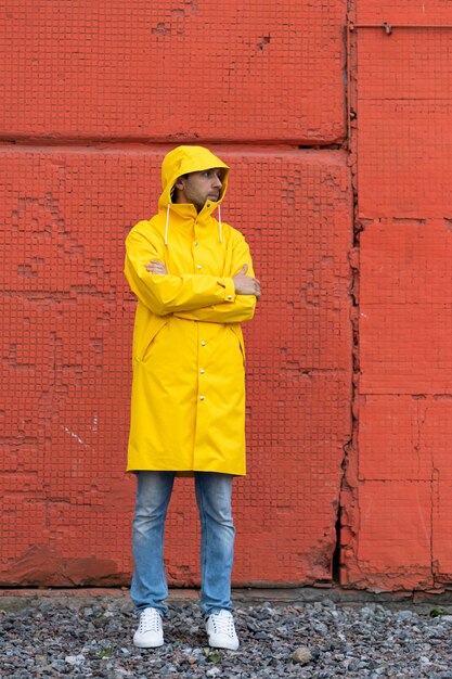 Homem com capa de chuva amarela perto de uma parede vermelha