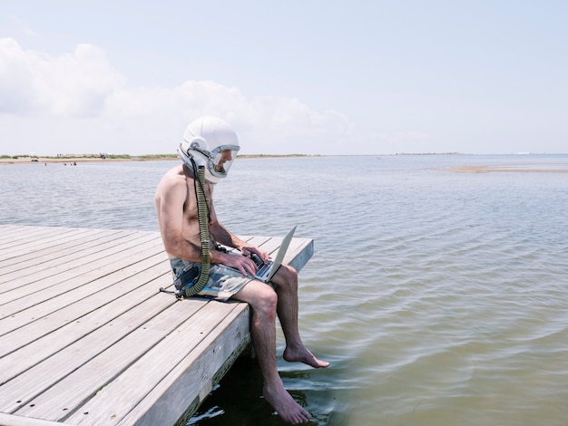 Homem com capacete de astronauta e laptop na praia