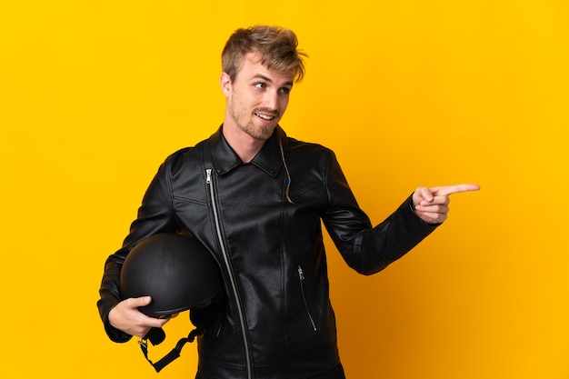 Homem com capacete de motociclista isolado em fundo amarelo apontando o dedo para o lado e apresentando um produto